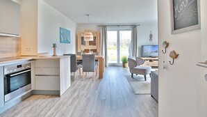 Moderni keittiö, jossa on sisäänrakennettu uuni, ruokailutila pöydän ja tuolien kera, televisio ja suuri ikkuna, jossa on verhot.
