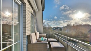 A balcony with wicker furniture, a table, and a view of the neighborhood. - Parkdomizil Appartement 9 (Scharbeutz)