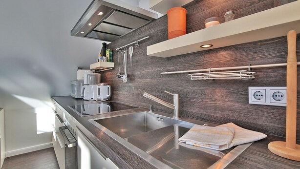 A modern kitchen with stainless steel appliances, wooden wall paneling, and built-in shelves. - Parkdomizil Appartement 9 (Scharbeutz)
