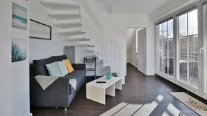 A modern living room with a dark grey sofa, white coffee table, and a staircase leading to another level. - Parkdomizil Appartement 9 (Scharbeutz)
