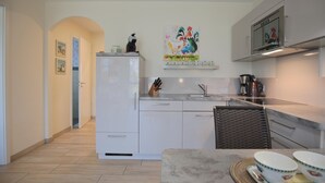 Cozinha moderna com armários brancos, bancada de mármore e um quadro sobre a pia.