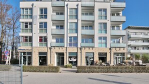 Um hotel de vários andares com design moderno, com varandas em cada andar, um restaurante no nível da rua e uma placa visível de um estabelecimento próximo.