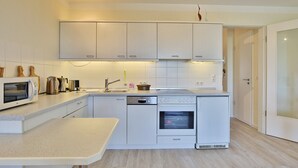 Una cocina moderna con armarios blancos, horno empotrado, microondas y lavavajillas.