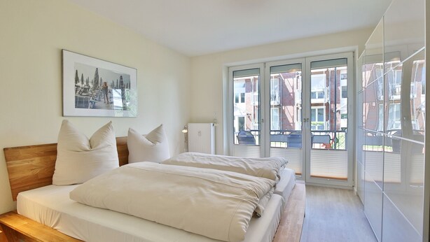 Un dormitorio con una cama grande, un cuadro en la pared y vistas al balcón exterior.