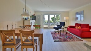 Amplia sala de estar con mesa de comedor de madera, sofá rojo y un gran ventanal con vistas al exterior.