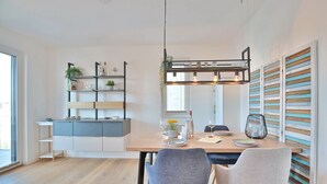 A modern kitchen with a central island, wooden flooring, and a dining area with two chairs. - Ferienwohnung Dünenblick App. 1 (Scharbeutz)