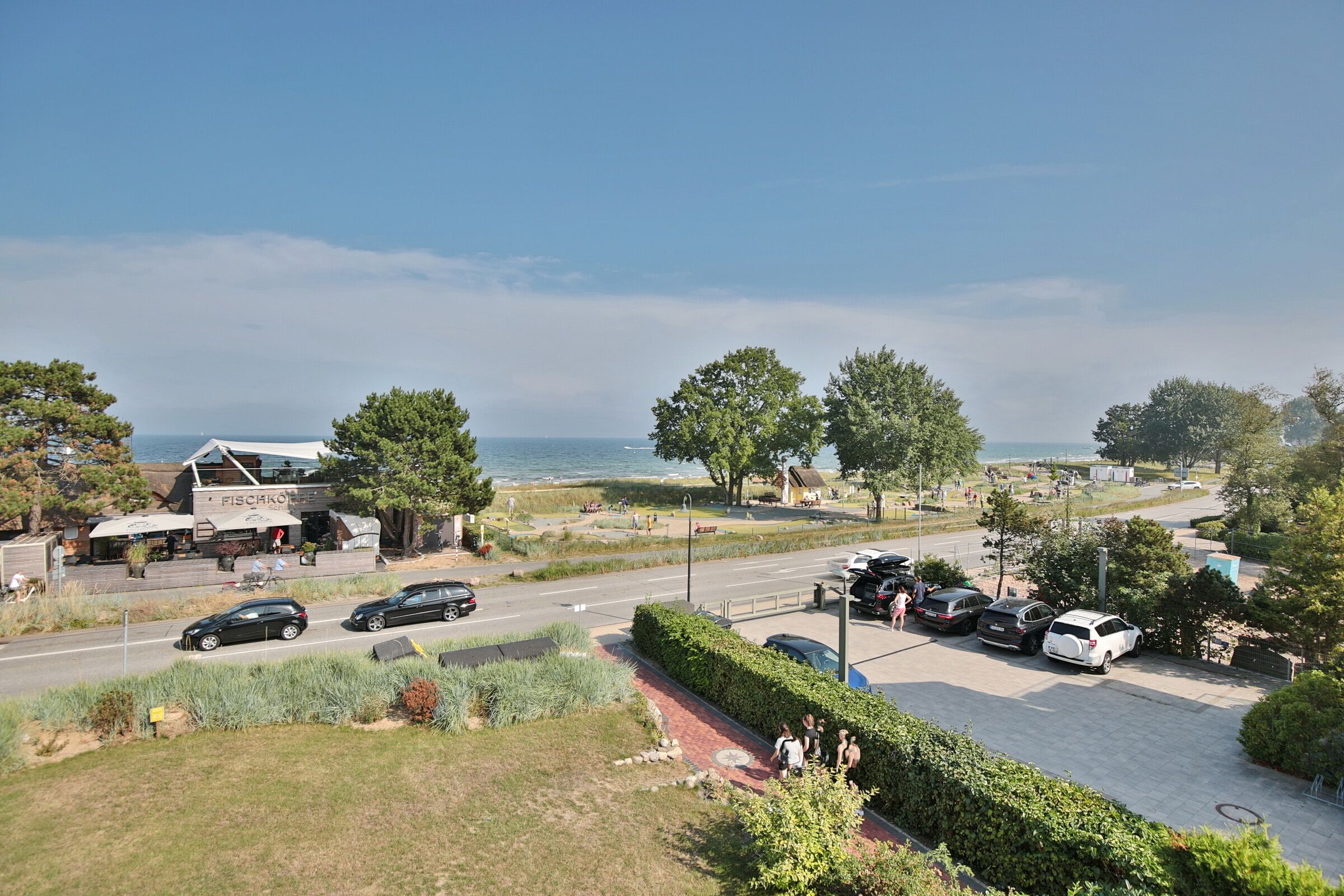 A coastal area with a restaurant, parked cars, and a pedestrian path.