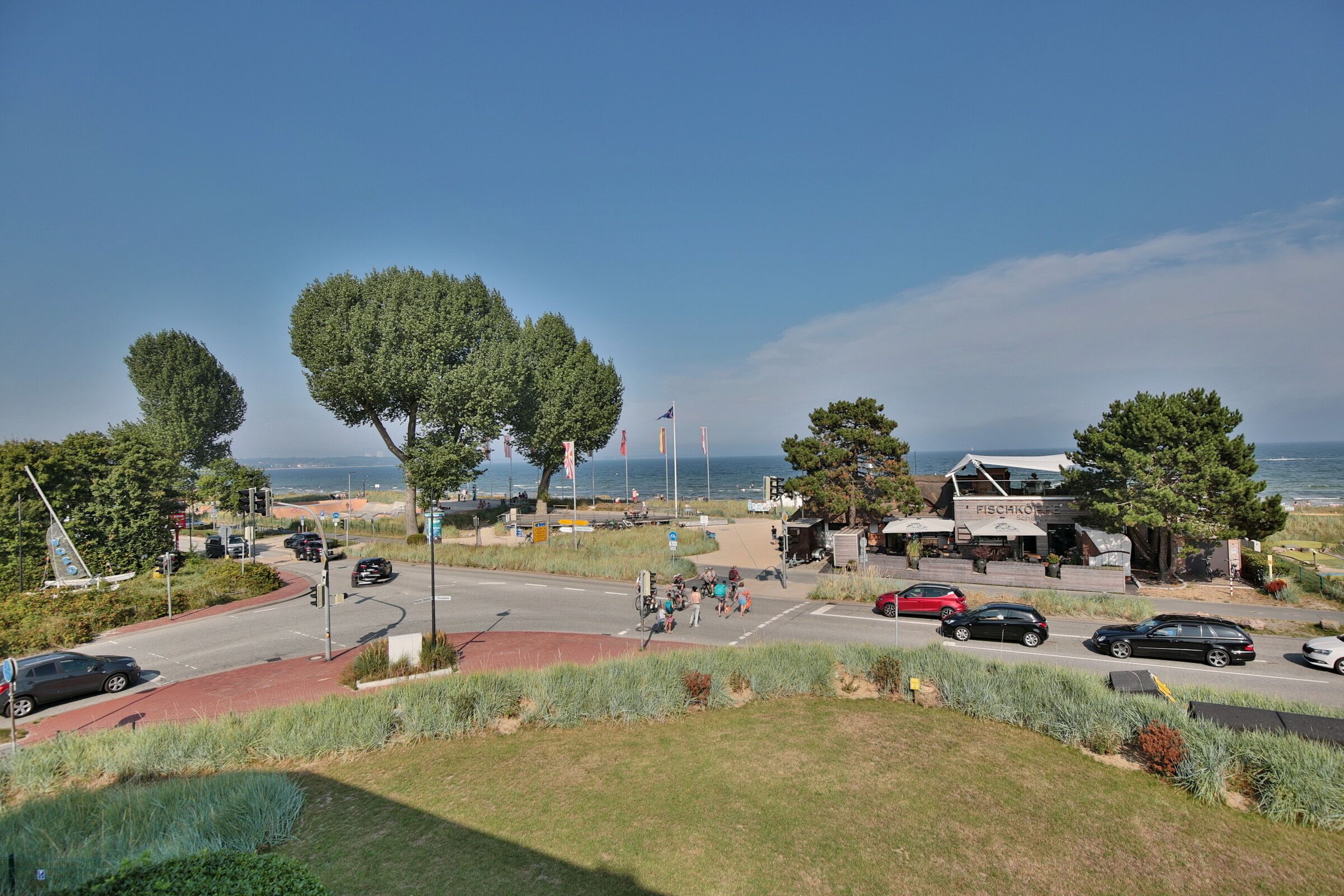 Eine Küstenstraße mit einem Restaurant namens 'FISCHKOFER' und Blick aufs Meer.