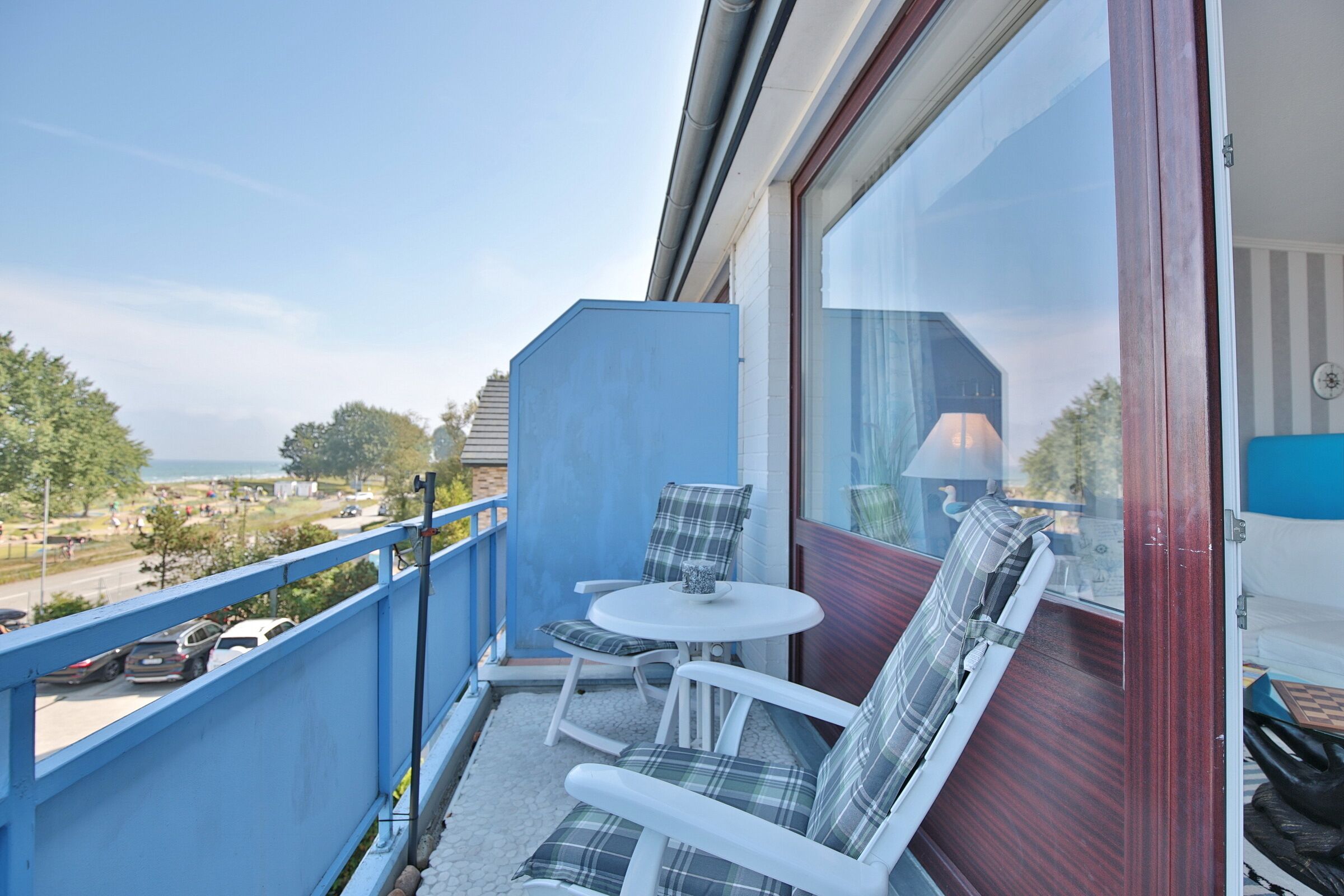 Un balcon avec une balustrade bleue, deux chaises blanches, une petite table ronde et une vue sur la mer.