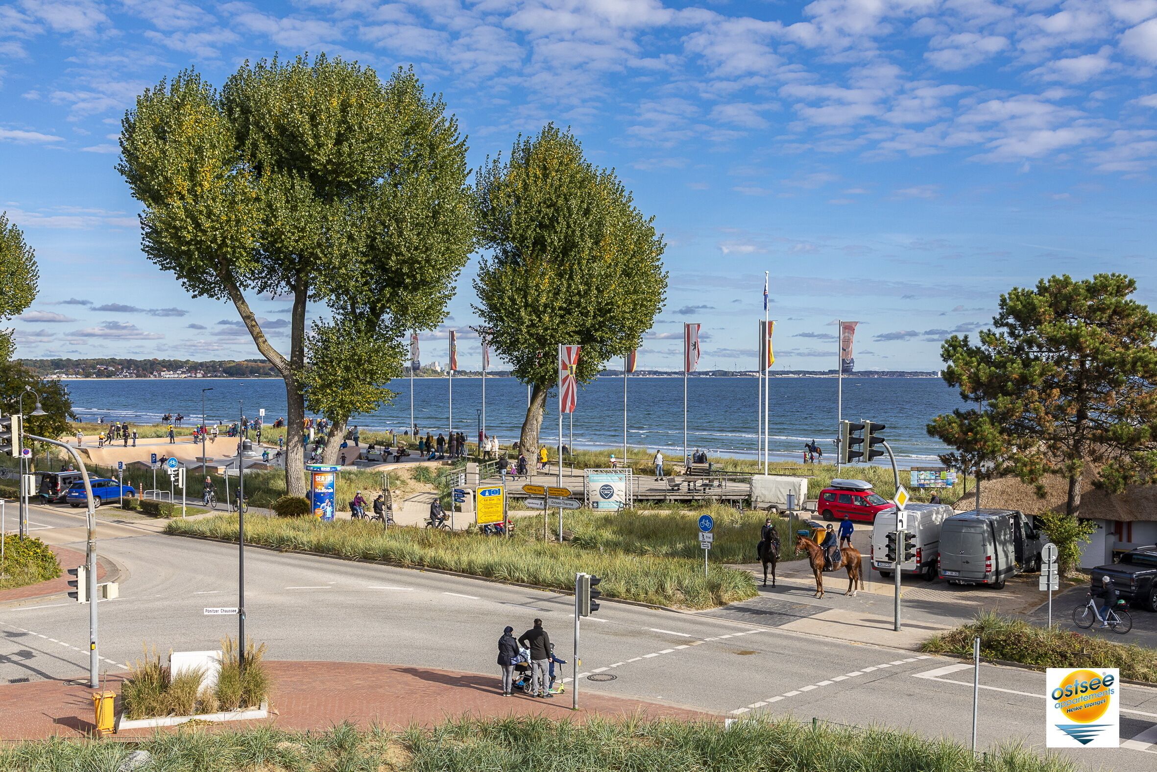 A coastal road with a beach in the background, traffic lights, and a few pedestrians.