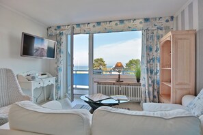 Ein modernes Wohnzimmer mit einer Couch, einem Glastisch, einem Fernseher und Meerblick durch große Fenster.