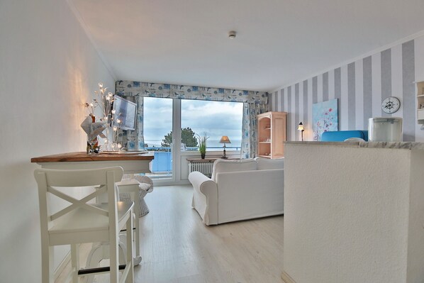 Uma sala de estar moderna com uma janela grande, um sofá branco, um armário de madeira e um espaço de jantar com uma cadeira e mesa brancas.