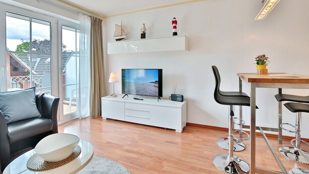 A modern living room with a sofa, TV, and a dining area with chairs. - Residenz Alte Bergstraße Appartement 14 (Scharbeutz)