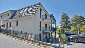Een modern gebouw met twee verdiepingen, een plat dak, balkons en een verharde oprit.