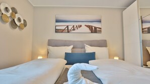Een hotelkamer met twee bedden, een groot schilderij van een strandpromenade en een decoratief wandobject.