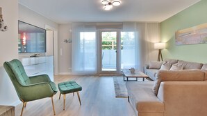 Een moderne woonkamer met een groene fauteuil, een beige bank en een flatscreen televisie.