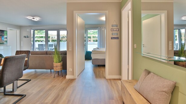 Een moderne woonkamer met een bank, eettafel en stoelen. Een hal leidt naar een slaapkamer met een bed en een badkamer.
