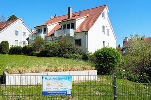 A two-story residential building with a red-tiled roof, a balcony, and a sign indicating the property is for sale.