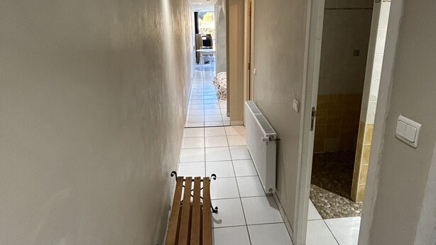 A hallway with a wooden bench, white tiled flooring, and a view into a room with a tiled shower area. - AGREABLE STUDIO Cabine au coeur de la station 5 bleuets (Besse-et-Saint-Anastaise)