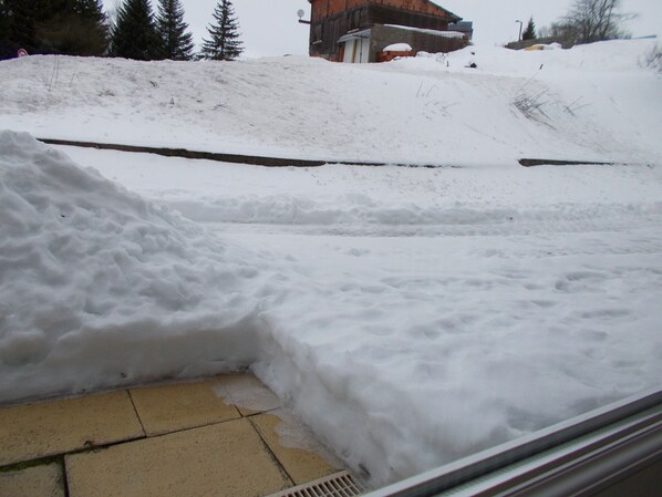 Schneebedeckte Landschaft mit einem Schneehaufen im Vordergrund und einem Gebäude im Hintergrund.