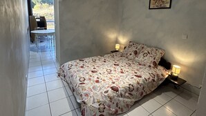 A bedroom with a bed, two bedside lamps, a picture on the wall, and a view of a dining area with chairs and a table. - AGREABLE STUDIO Cabine au coeur de la station 5 bleuets (Besse-et-Saint-Anastaise)