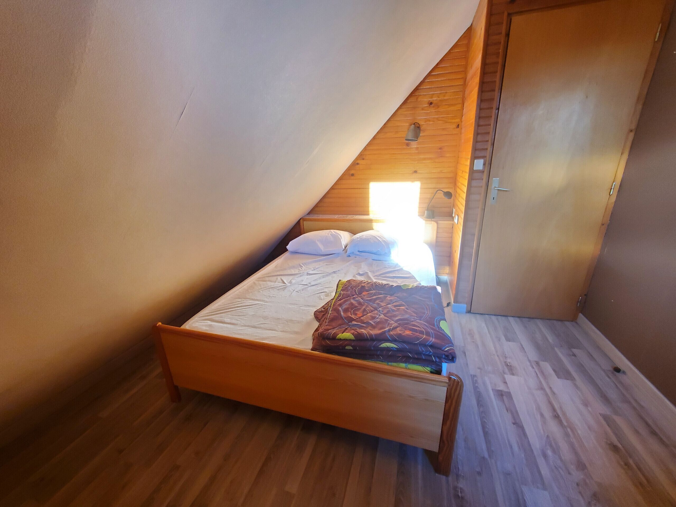 A small, single-bed room with a sloped ceiling, wooden flooring, and a door to the right.