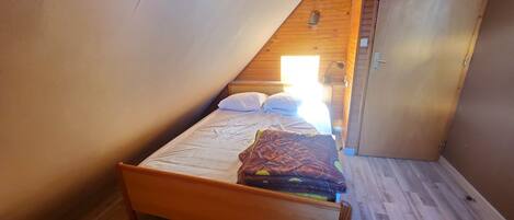 A small, single-bed room with a sloped ceiling, wooden flooring, and a door to the right.