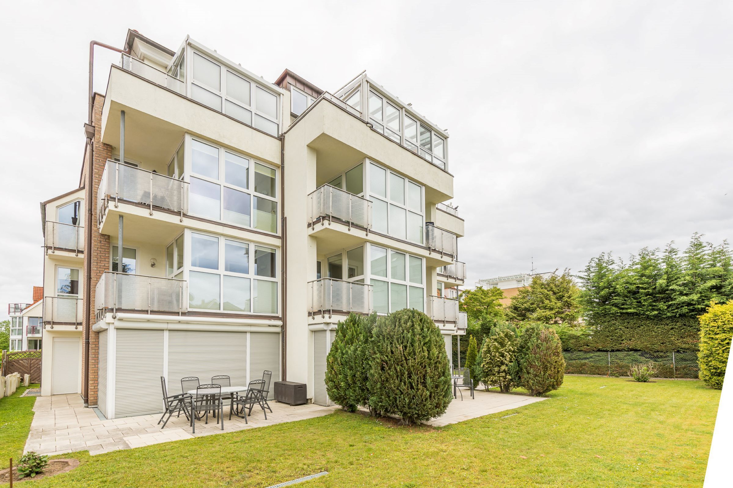 A multi-story residential building with balconies, a patio area with outdoor furniture, and a well-maintained lawn.