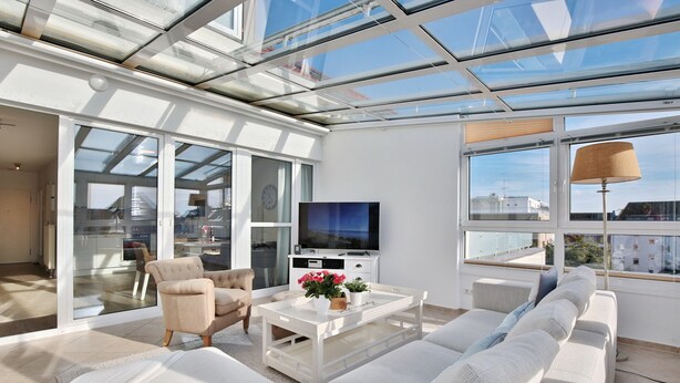 A modern living room with a glass ceiling, a flat-screen TV, a sofa, and a coffee table with decorative items. - Haus Seesand Hansastrasse 7, Penthouse Wohlfühlzeit (Scharbeutz)