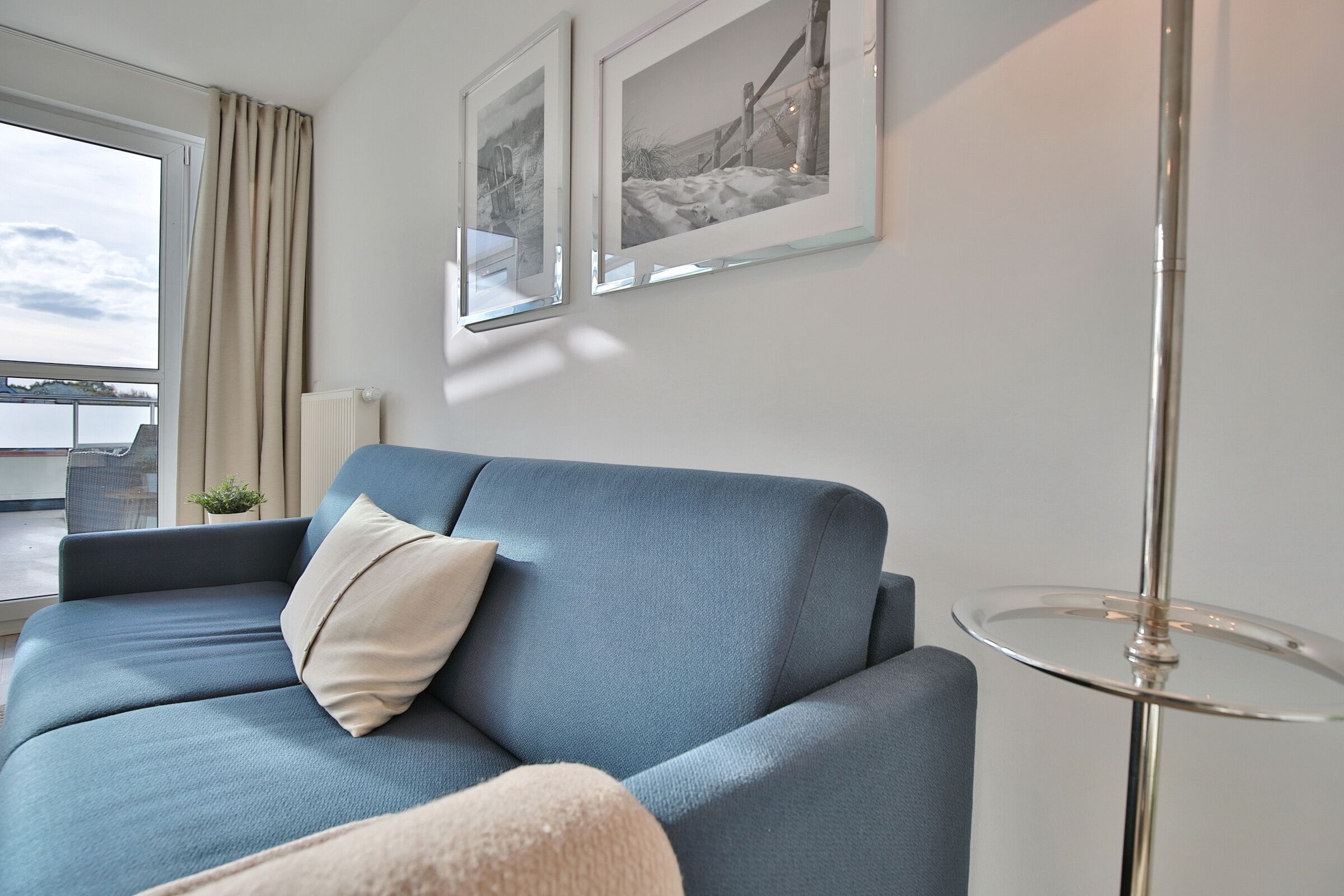 A modern living room with a blue sofa, a small round table, and two framed pictures on the wall.
