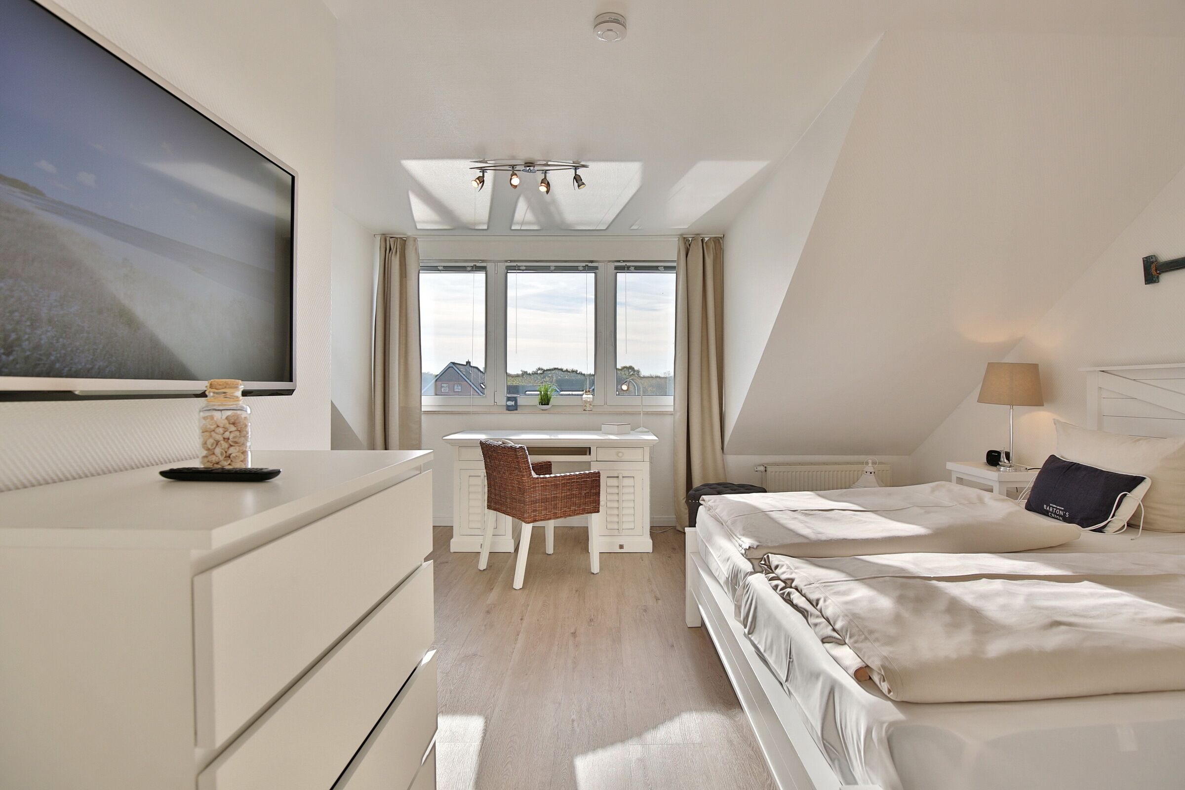 Quarto de hotel moderno com uma cama grande, uma escrivaninha e vista da cidade por grandes janelas.