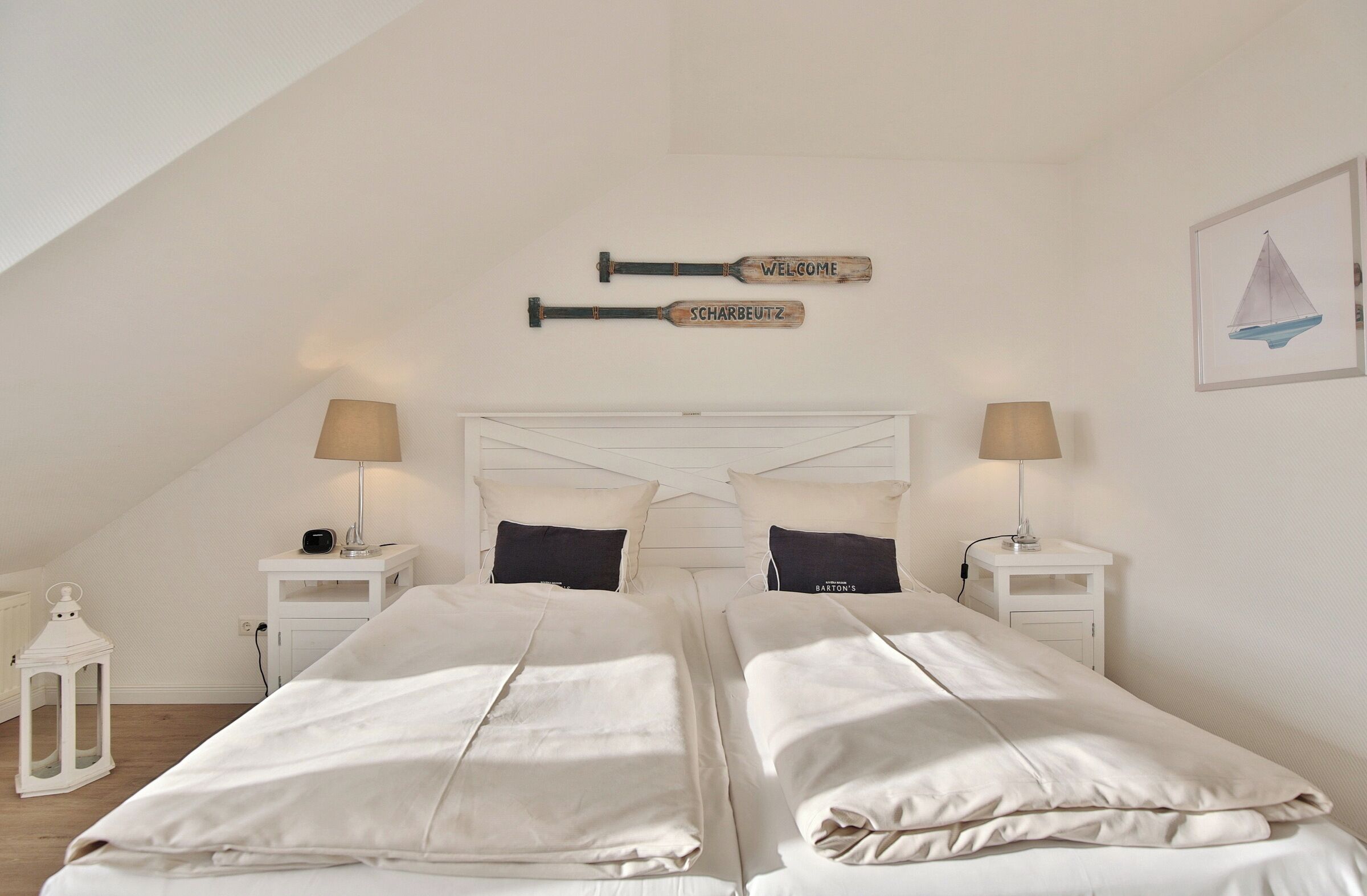 Un dormitorio con dos camas, ropa de cama blanca, cabecero de madera y una pintura de un velero en la pared.