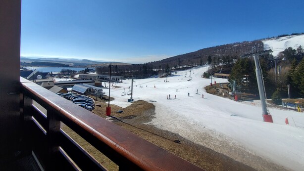 Une station de ski dotée d’un télésiège, de pistes de ski et offrant une vue sur un lac et des montagnes.