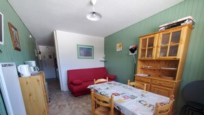 Une pièce de taille modeste comprenant une table à manger, des chaises, un canapé rouge, un meuble en bois et un coin cuisine.