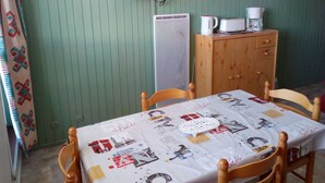 Un coin repas avec une table recouverte d’une nappe aux motifs parisiens, une horloge, un téléviseur et un meuble contenant une machine à café.