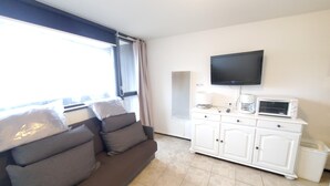 Ein Wohnzimmer mit einer Couch, einem Flachbildfernseher, einer Kaffeemaschine und einem Mülleimer.