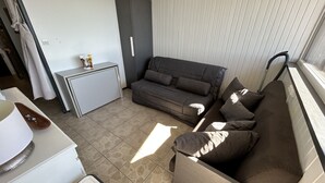 Ein kompakter Wohnbereich mit einer Couch, einer kleinen Küchenzeile und einem Fenster mit Jalousien.