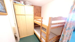 Quarto com beliches, um guarda-roupa de madeira e um tapete verde.