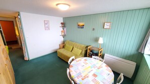 Um quarto acolhedor com parede verde, um sofá estampado, uma mesa pequena com toalha de mesa colorida e uma luminária.