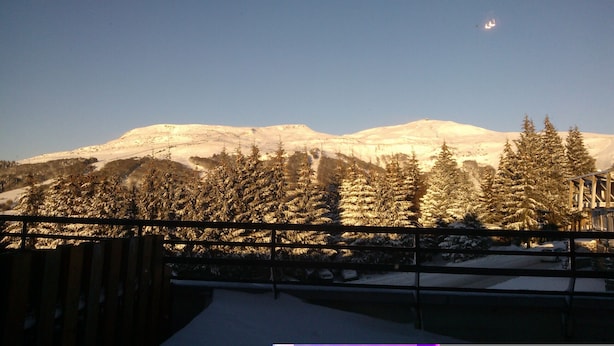 A snowy mountain landscape with a clear sky, viewed from a balcony with a railing.