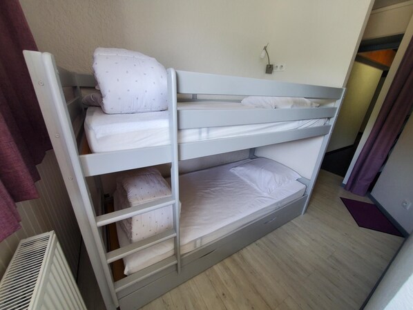 A bunk bed with two levels, a white radiator, and a light switch on the wall.
