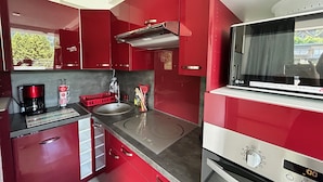 A modern kitchen with red cabinets, a stainless steel sink, a coffee maker, and a microwave.