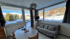A cozy room with a round table, a sofa, and a window with a view of a snowy landscape.
