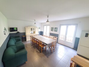 A spacious living area with a dining table, chairs, a sofa, and a kitchen area with a refrigerator.