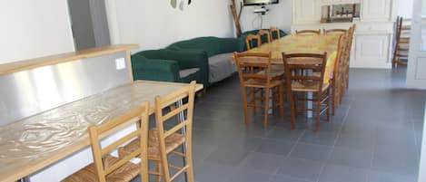 A dining area with a long wooden table and chairs, a green sofa, and a television mounted on the wall.