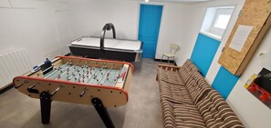 Una habitación con mesa de fútbol, sofá, sillón y ventana.