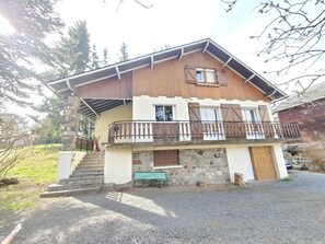 Un chalet de dos pisos con base de piedra, estructura superior de madera y un balcón con barandilla de metal.
