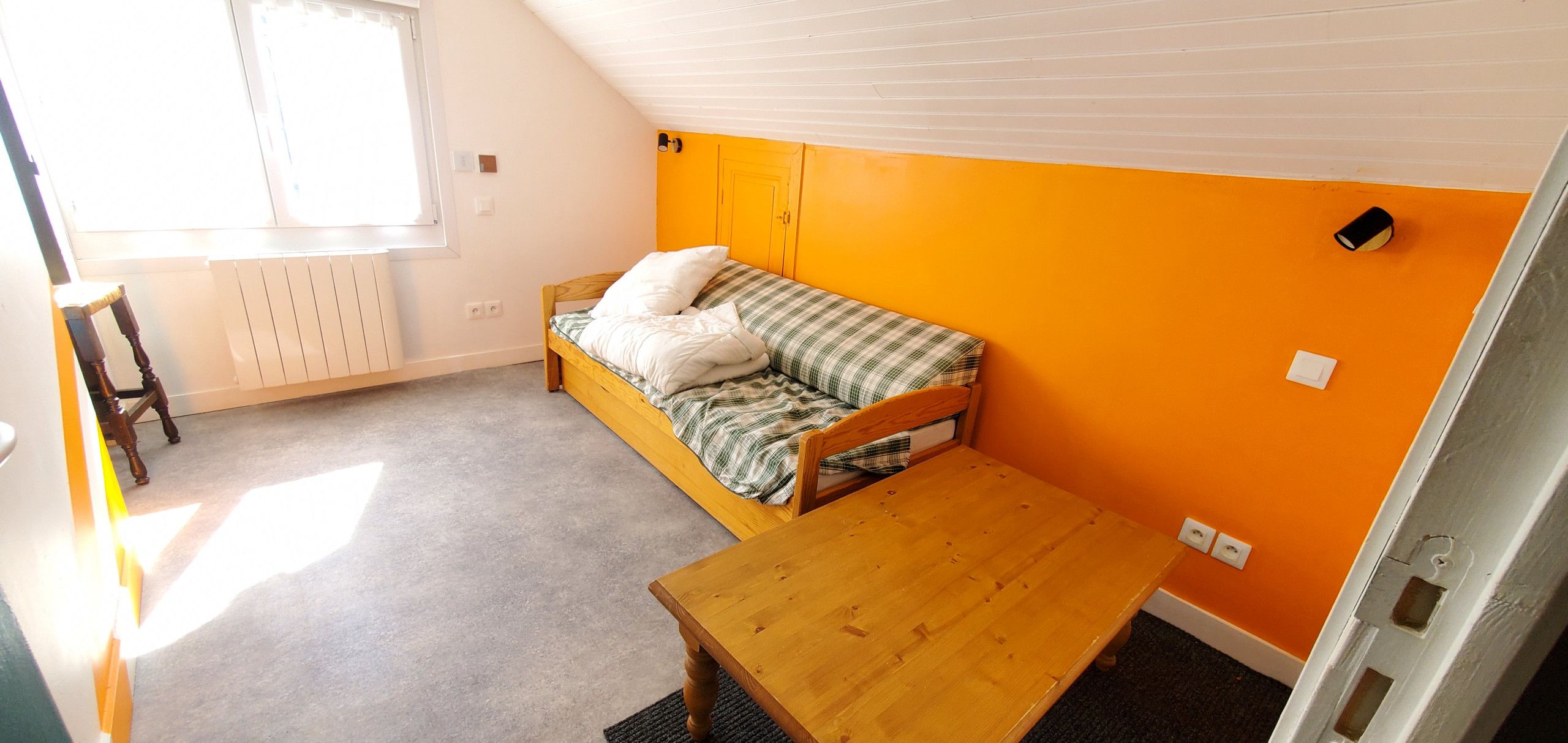 A room with a single bed, a wooden table, and a window.