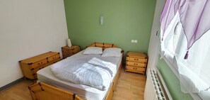 Un dormitorio con una cama, mesitas de noche de madera, un aparador y un radiador.