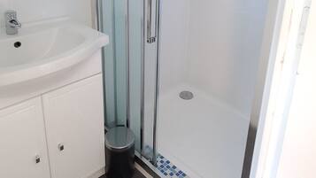 A bathroom with a glass-enclosed shower, a white sink, and a tiled floor.